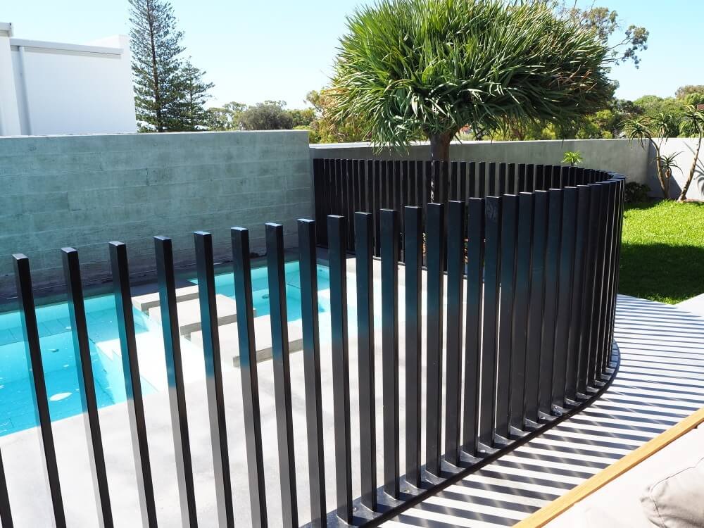 Black vertical batten fence beside a swimming pool.